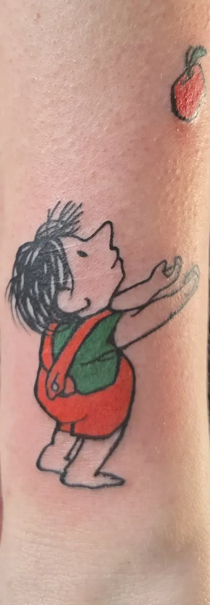 Small color cartoon figure tattoo reaching upward, placed on a wrist
