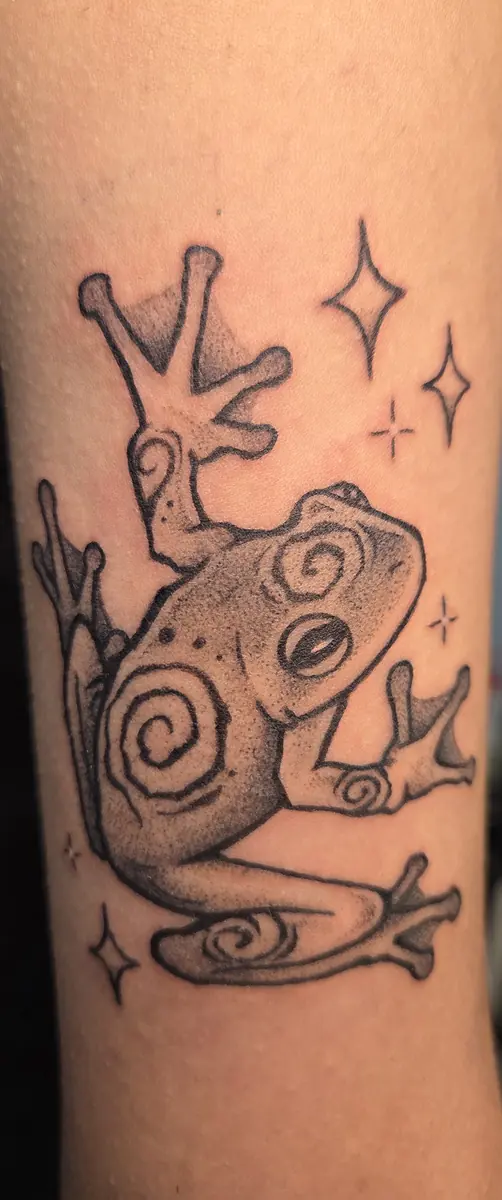 Black and grey frog tattoo with sparkle detailing on a forearm