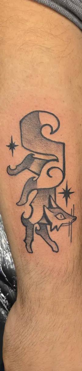 Small black and grey jester tattoo with sparkles on an arm