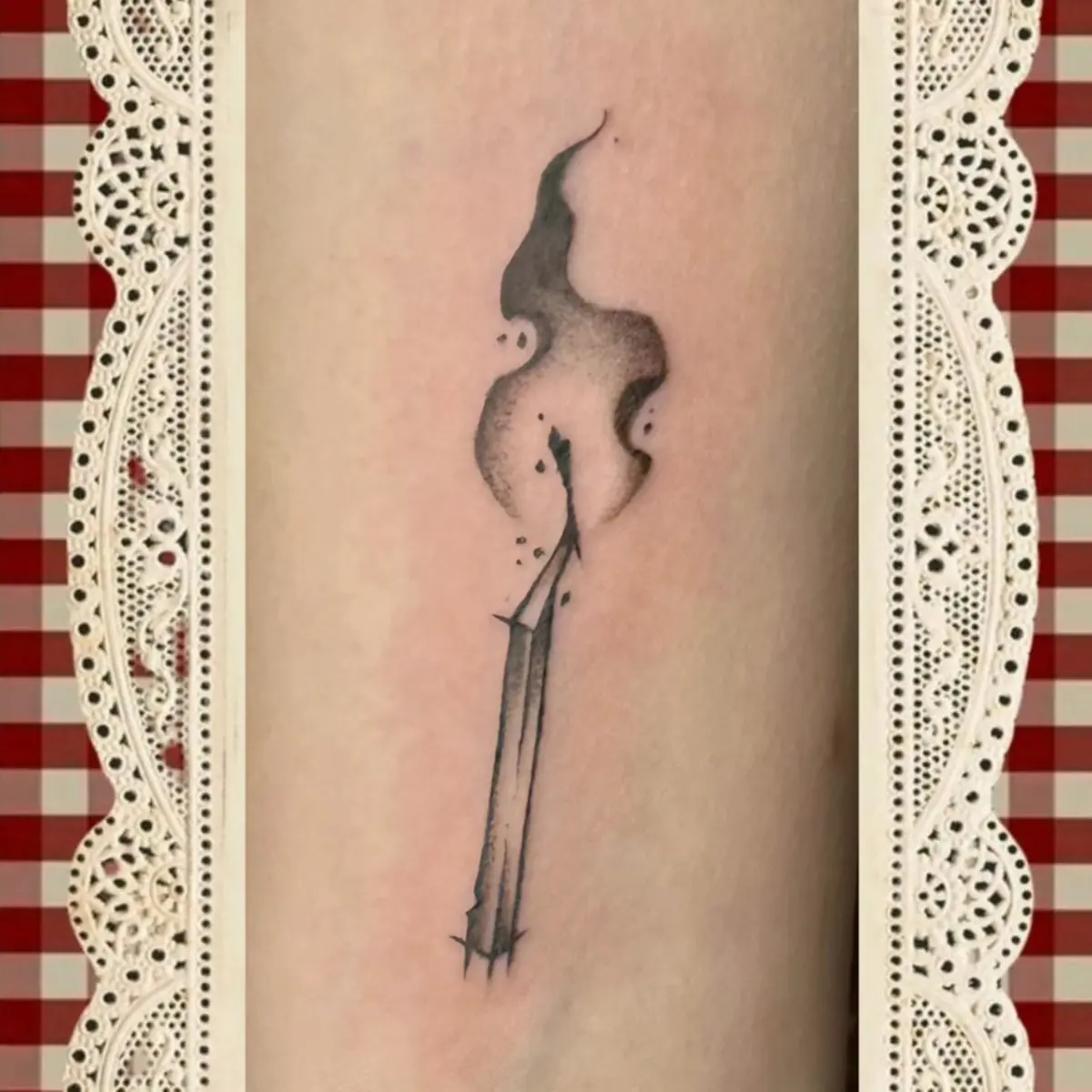 Black and grey tattoo of a lit match with curling smoke on an arm