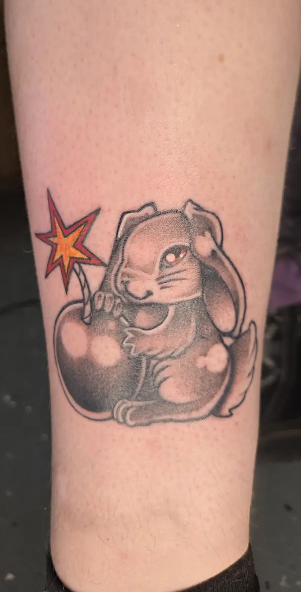 Black and grey tattoo of a rabbit holding a star wand on a calf