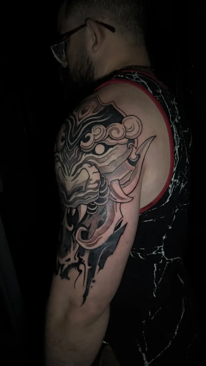 Black and grey Japanese mask tattoo across a shoulder and upper arm