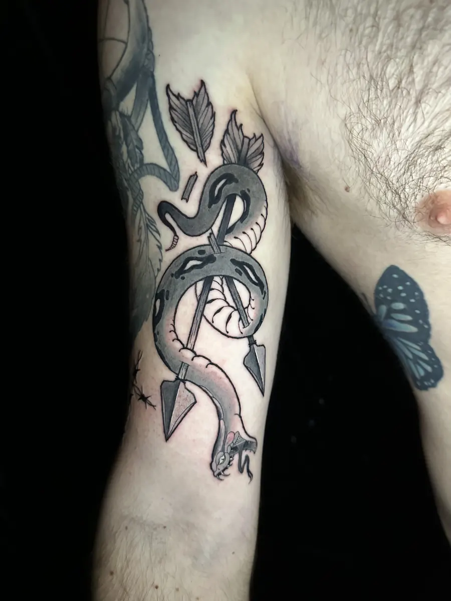 Black and grey tattoo of a snake coiled around arrows on an inner arm