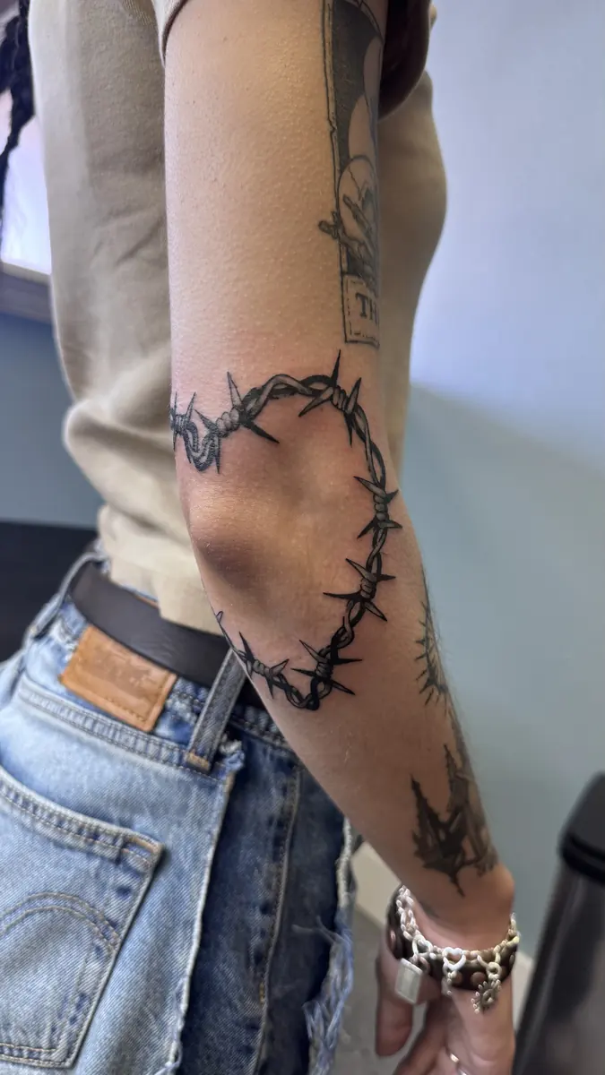 Blackwork barbed wire tattoo wrapping an arm and hand