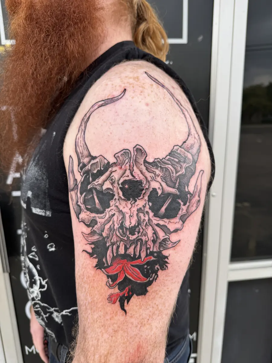 Blackwork horned demon skull tattoo with a red accent on an upper arm