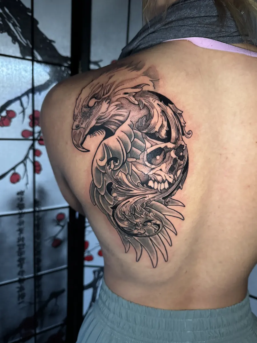Blackwork back tattoo of a coiled serpent, skull and flowers across a shoulder blade