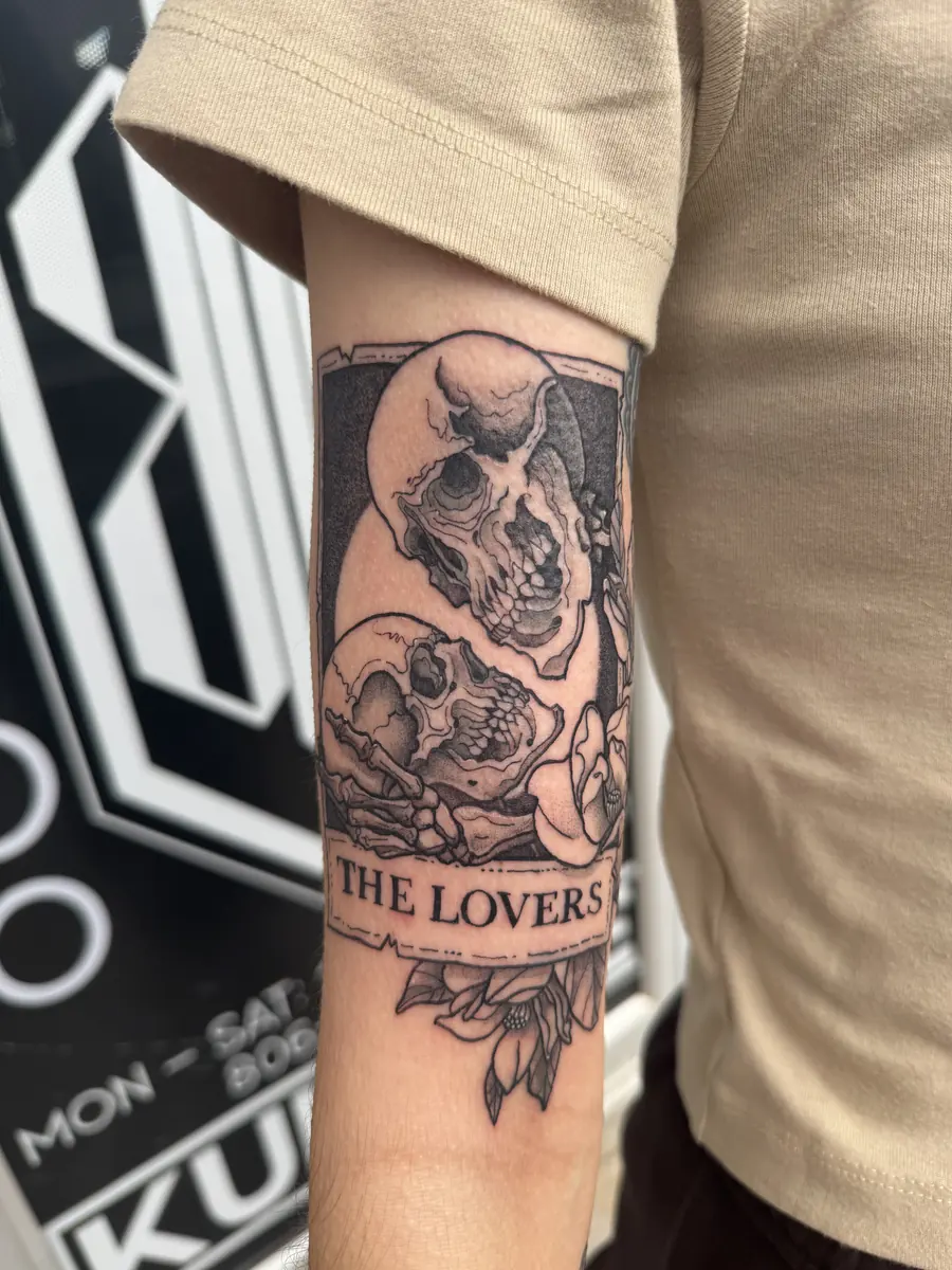 Blackwork tarot card tattoo of two skulls labelled The Lovers on an inner arm, tattooed at Blind Fox Tattoo in Amarillo, TX