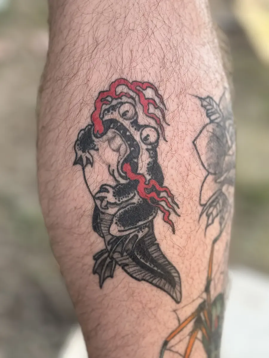 Neo-Japanese tattoo in solid black with red accents on a calf