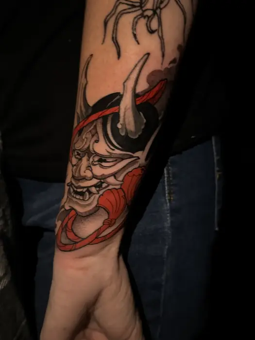 Japanese hannya mask tattoo in black, red and orange on a forearm