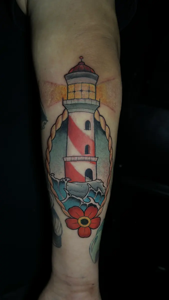Neo-traditional lighthouse tattoo with a red flower on a forearm