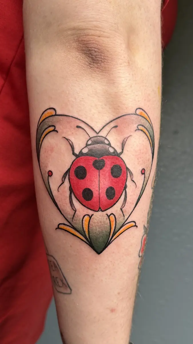 Traditional ladybug tattoo framed in a cream art-nouveau shape on a forearm