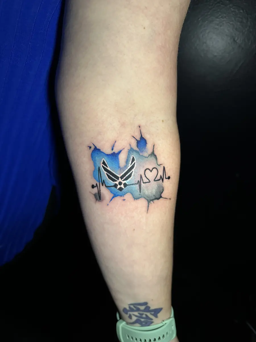 Air Force emblem tattoo over a blue watercolor splash on an arm